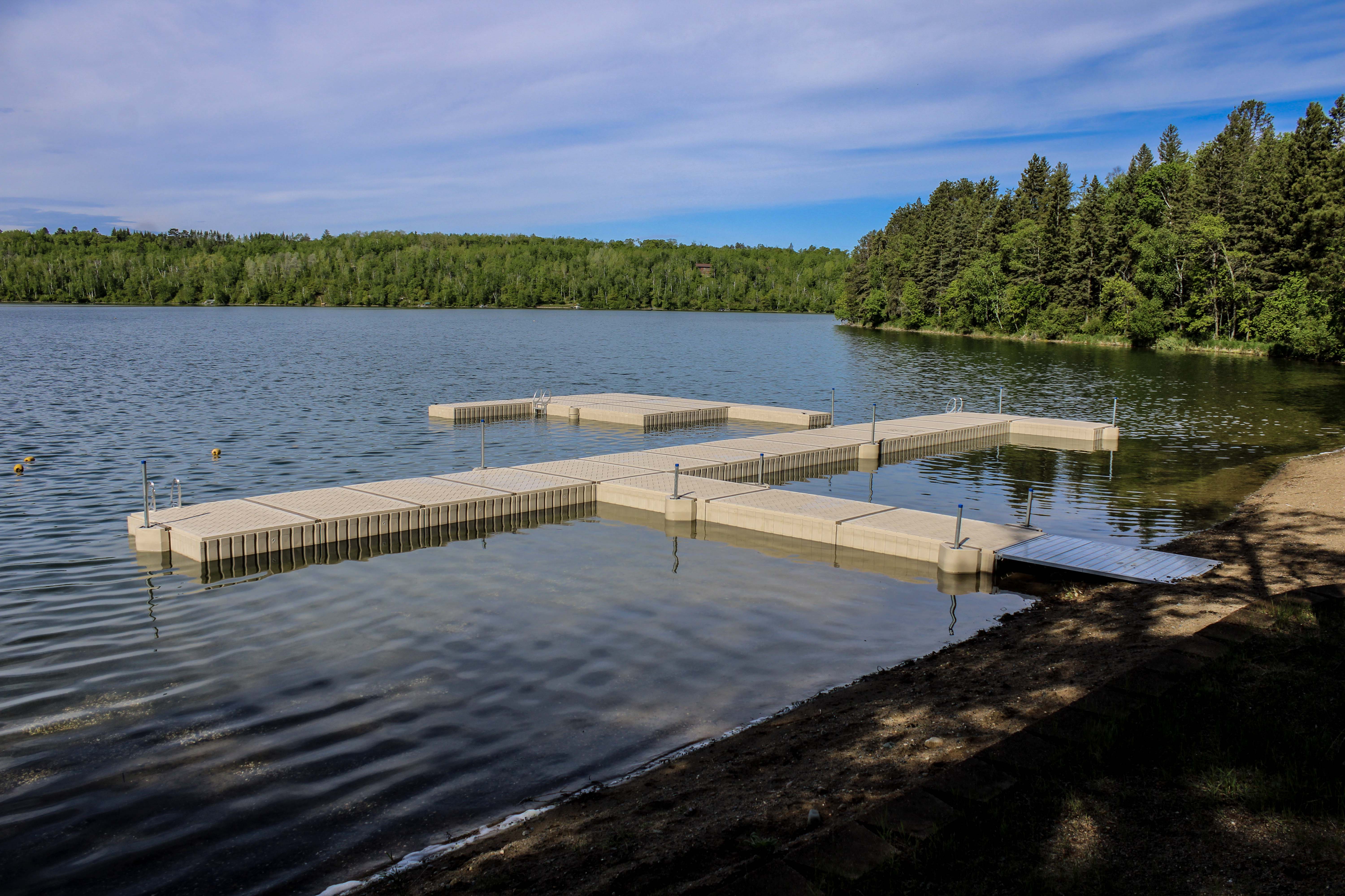 Modular floating dock system extending into a calm lake surrounded by a forested shoreline.