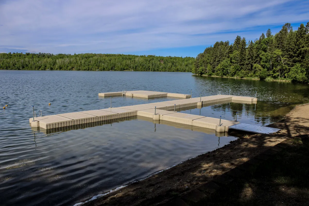 Modular floating dock system extending into a calm lake surrounded by a forested shoreline.