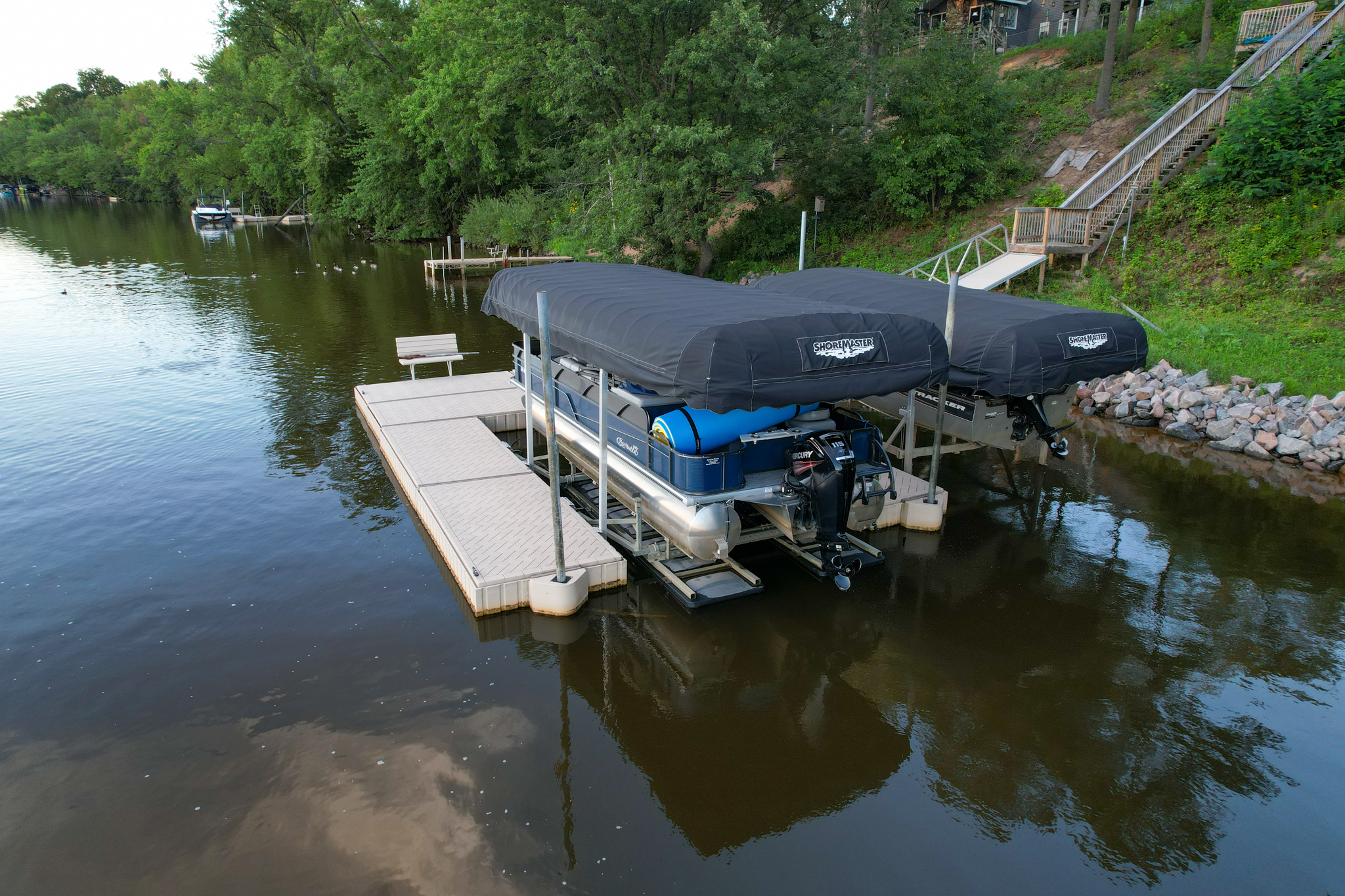 Two boats in boat lifts docked on a lake next to a floating dock system