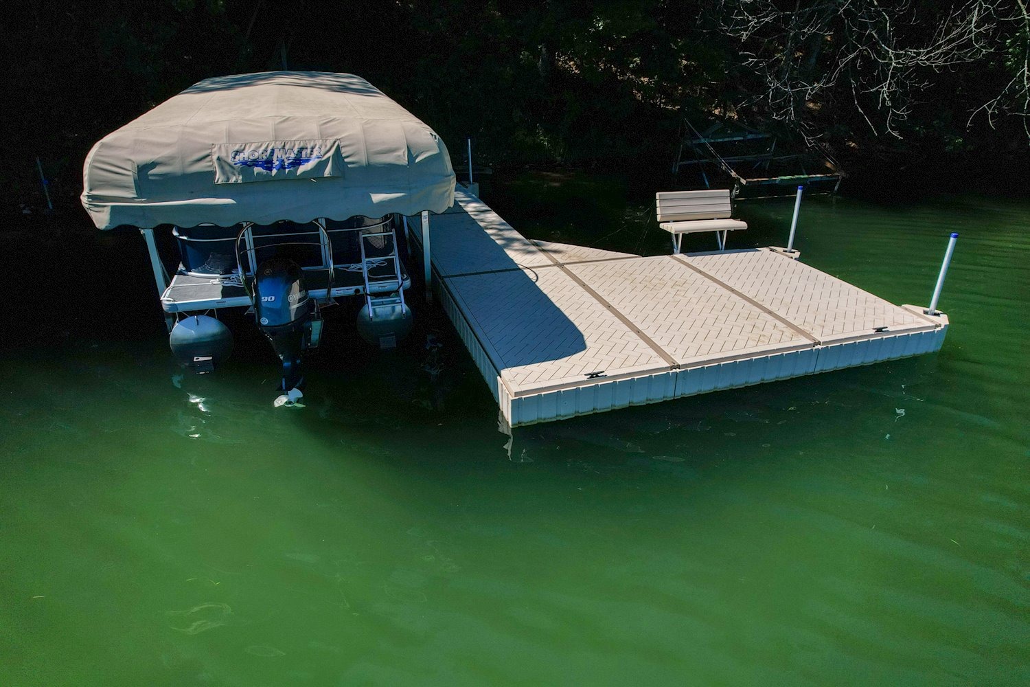 Covered pontoon boat on a HydroHoist boat lift beside a large floating dock on a lake.
